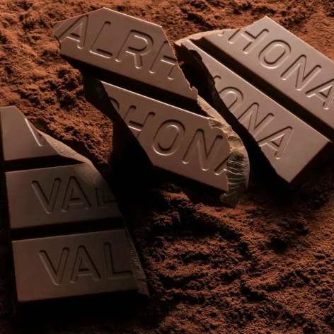Broken Valrhona Amatika 46% plant-based chocolate block on a bed of cocoa powder